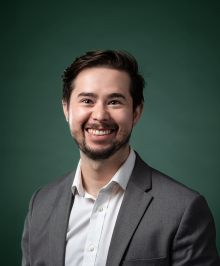 Christopher in a gray suit and a white shirt smiling in front of a green background